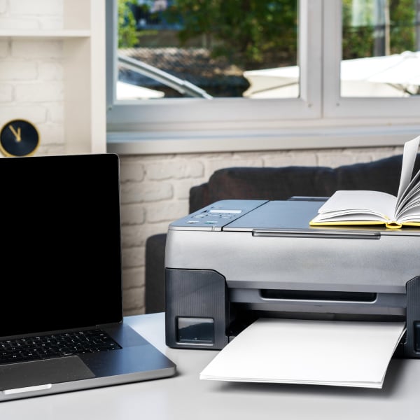 Imprimante jet d�encre install�e dans un bureau � domicile, � c�t� d�un ordinateur portable, avec une feuille en cours d�impression.