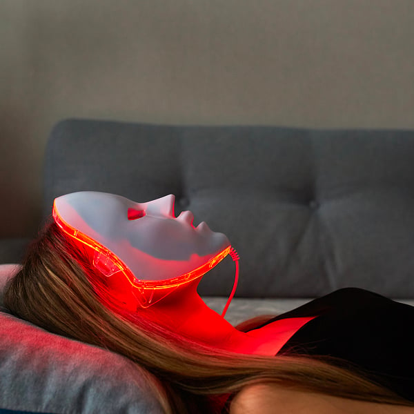 Een vrouw licht in de zetel met een LED-masker met rood licht