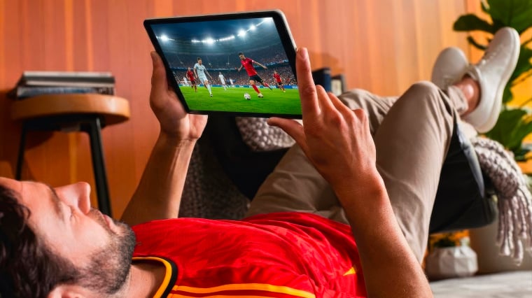 Een man ligt op bed naar voetbal te kijken op zijn tablet