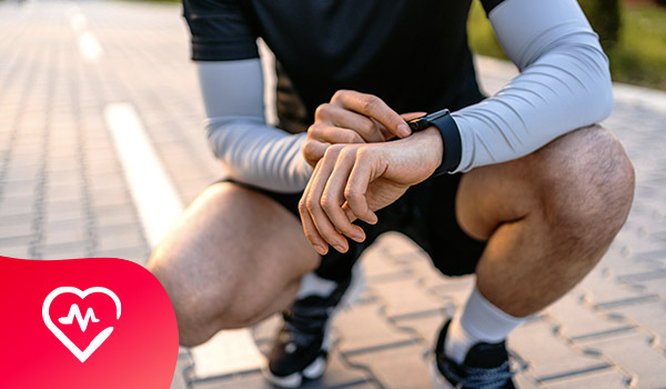 Een man in sportieve kledij hurkt om zijn smartwatch te raadplegen.
