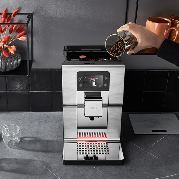 Une personne qui met des grains de caf dans la machine  caf Krups Intuition Experience + 