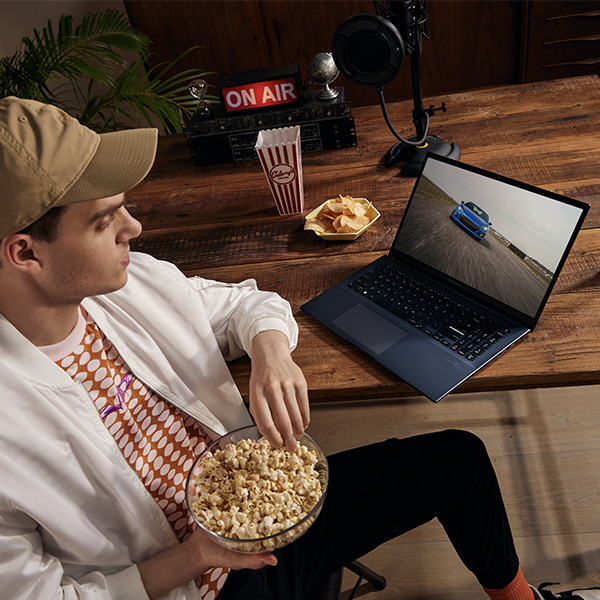 Een man die een video bekijkt op zijn Asus Vivobook Pro 15 OLED-laptop terwijl hij popcorn eet 