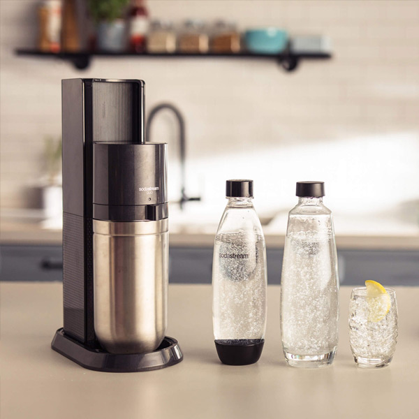 Un appareil Sodastream Duo Black, les deux bouteilles et un verre remplis d'eau gazeuse, dans une cuisine claire