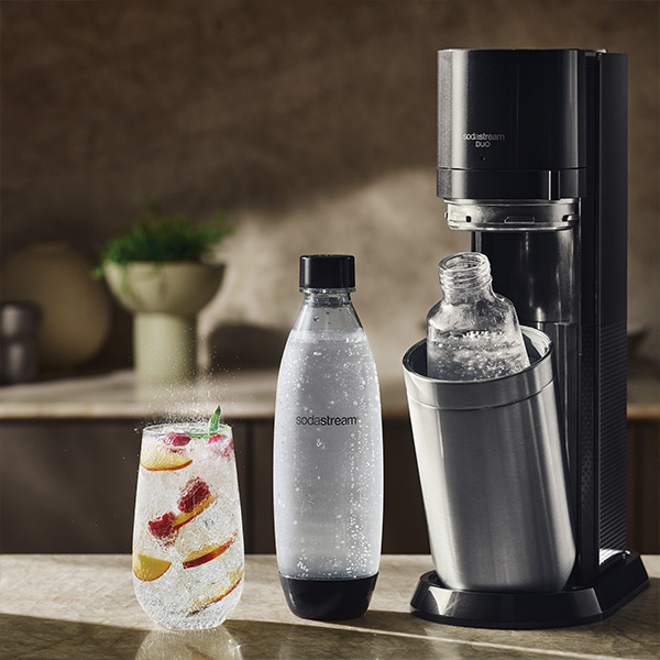 Zoom sur l'appareil Sodastream Duo Black, les deux bouteilles et un verre d'eau gazeuse remplis de fruits frais