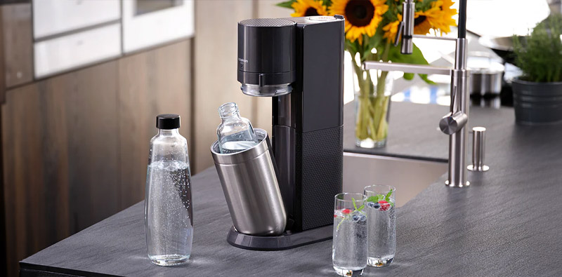 Un appareil Sodastream Duo Black, les deux bouteilles et deux verres remplis d'eau gazeuse, dans une cuisine claire