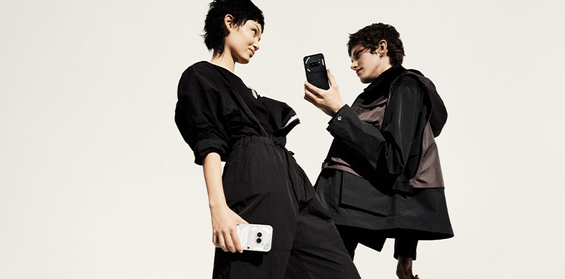 Een man en een vrouw gekleed in het zwart, elk met een Nothing Phone (2a) in de hand.