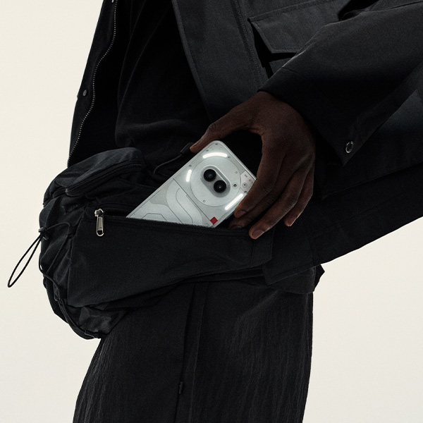 Een in het zwart geklede persoon haalt een witte Nothing Phone (2a) uit zijn tas.