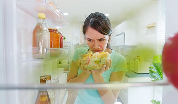 On voit le frigo de l'intrieur. Une dame sent un plat qui ne semble plus sentir bon.