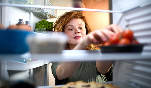 On voit le frigo de l'intrieur. Une personne souriante tend les mains vers des fraises.