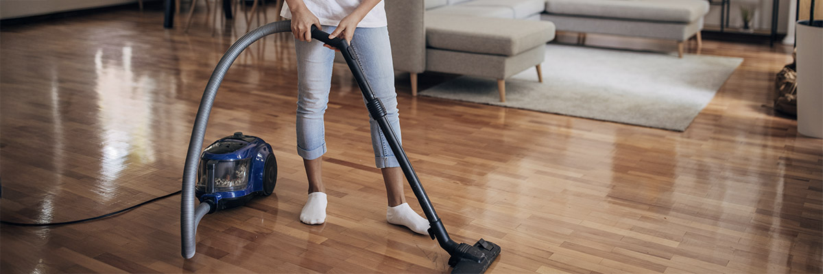 Een vrouw stofzuigt de parketvloer van haar woonkamer met een zakloze sledestofzuiger. 