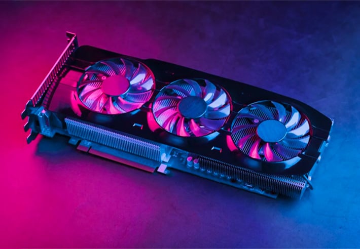 Carte graphique �quip�e de trois ventilateurs pos�e sur une surface sombre avec un �clairage rose � gauche et bleu � droite