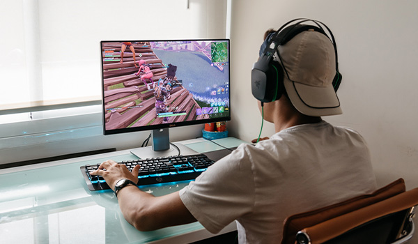 Personne assise � un bureau jouant � un jeu vid�o sur un �cran d�ordinateur, avec un casque audio et un clavier r�tro�clair�