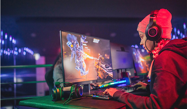 Personne assise � un poste de gaming utilisant un clavier et une souris devant un �cran affichant une sc�ne de jeu vid�o, avec un casque audio et un �clairage LED color� en arri�re‑plan