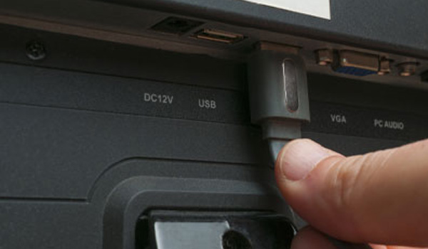 Main ins�rant un connecteur USB dans un port situ� � l�arri�re d�un appareil �lectronique comportant des �tiquettes DC12V, USB, VGA et PC AUDIO