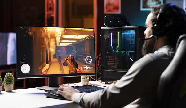 Personne assise � un bureau jouant � un jeu vid�o sur un �cran d�ordinateur, utilisant un clavier et une souris, avec une tour PC �clair�e en RGB � c�t�