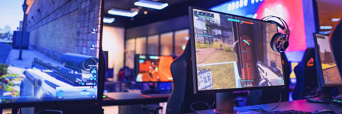 Rang�e de postes de gaming avec des �crans affichant une sc�ne de jeu vid�o en vue subjective et des casques suspendus, dans une salle �clair�e par des lumi�res color�es
