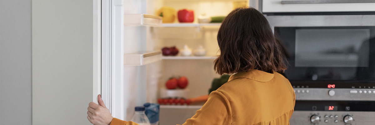 Vue de dos d�une personne ouvrant la porte d�un r�frig�rateur rempli d�aliments dans une cuisine avec un four et un micro‑ondes int�gr�s