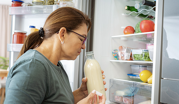 Personne tenant une bouteille en verre contenant un liquide clair et l�approchant de son nez devant un r�frig�rateur ouvert rempli d�aliments