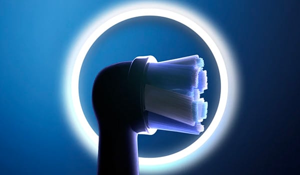 Close‑up van een opzetborstel van een elektrische tandenborstel, verlicht door een ronde lichtgevende halo op een blauwe achtergrond