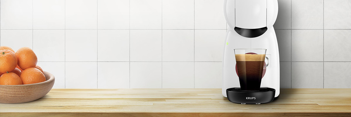 Machine � caf� Krups blanche pr�parant un espresso dans un verre, pos�e sur un plan de travail en bois avec un bol d�oranges � gauche.