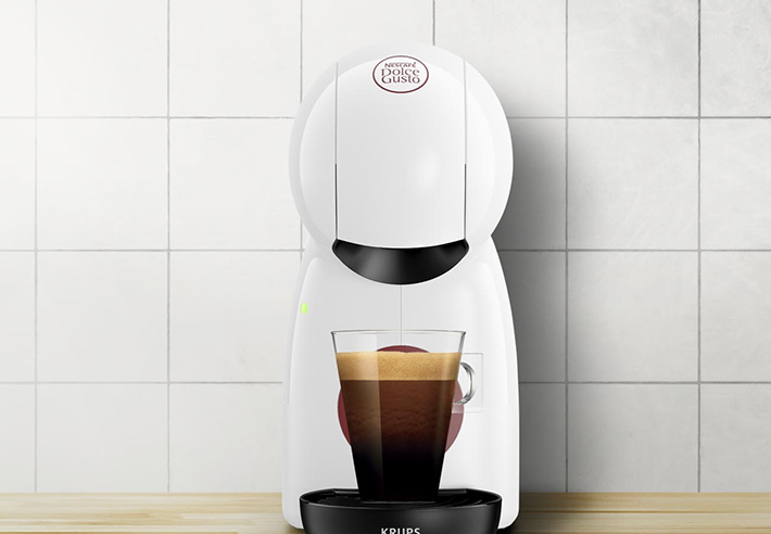 Machine � caf� Krups blanche pr�parant un espresso dans un verre, pos�e sur un plan de travail en bois avec un bol d�oranges � gauche.
