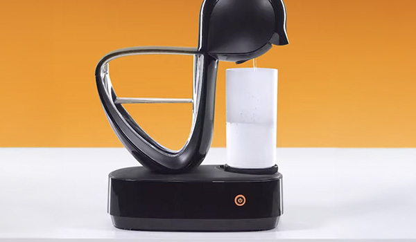 Machine � caf� noire d�pos�e sur une base, en train de verser un liquide dans un r�cipient cylindrique transparent, sur un fond orange.