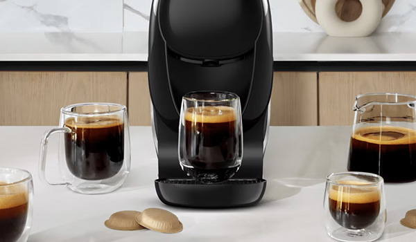 Machine � caf� noire plac�e sur un plan de travail, entour�e de plusieurs verres transparents remplis de caf� et de biscuits pos�s � l�avant.