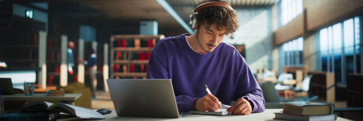Persoon gebruikt een laptop en maakt notities in een bibliotheek.