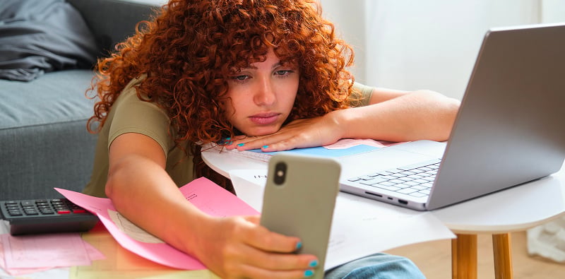 Persoon kijkt naar een smartphone voor een laptop.
