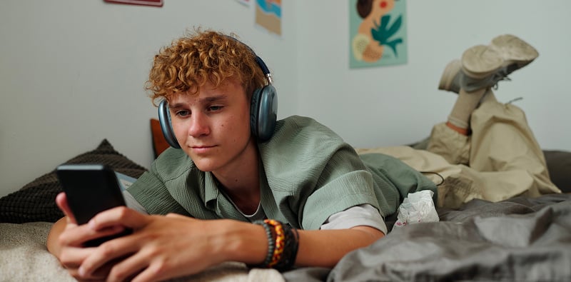 Persoon gebruikt een smartphone terwijl die met een hoofdtelefoon op bed ligt.