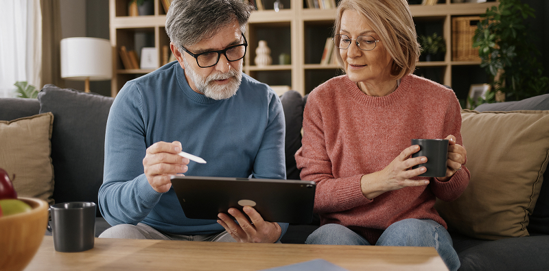 Twee personen zitten op een bank en bekijken samen een tablet in een gezellige woonkamer.