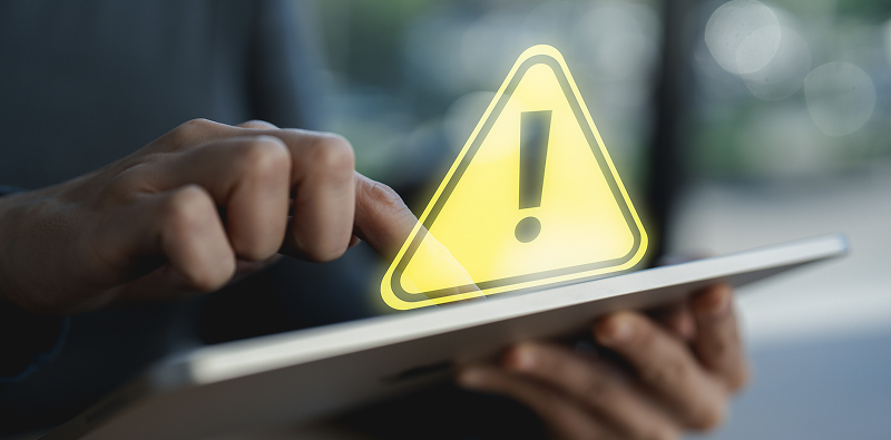 Hand die een tablet gebruikt met een waarschuwingspictogram op de voorgrond.